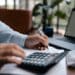 Free A person calculating finances with a calculator and pen on a desk indoors. Stock Photo